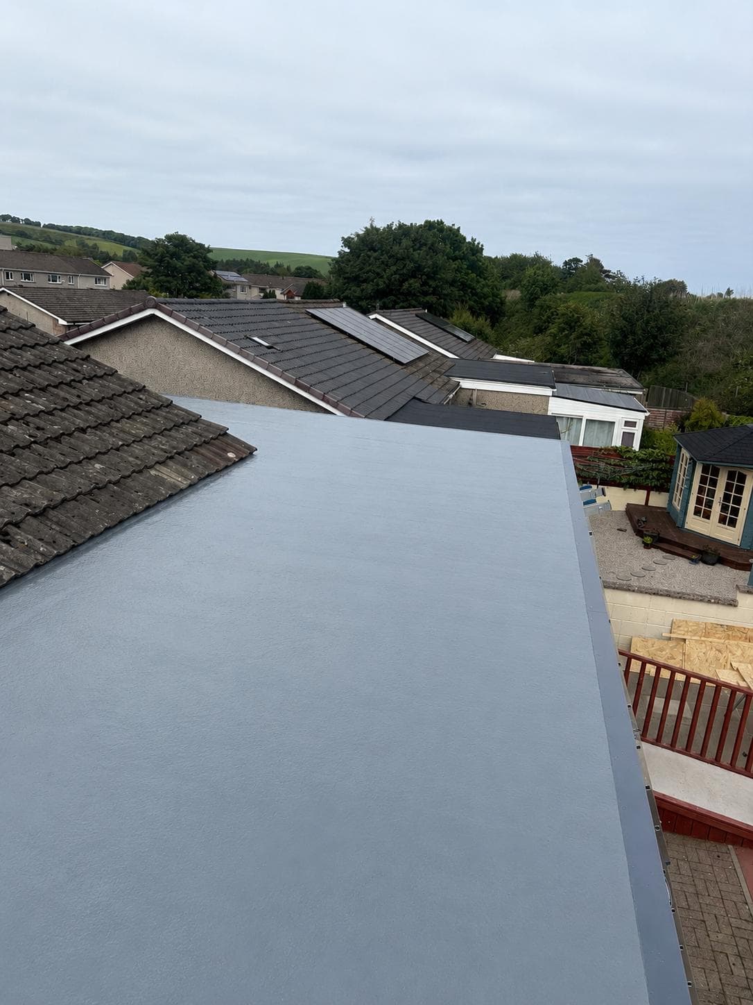 Grey flat roof surface with perimeter trims beside a tiled roof